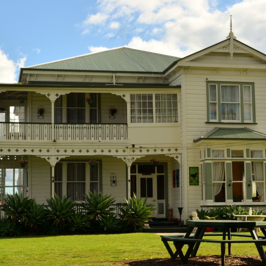 A cream two-storey villa with deep verandas, a green roof and a picnic table on the lawn