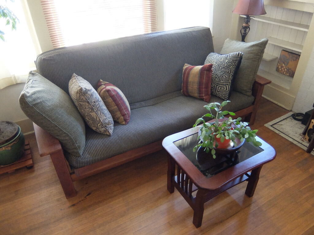 A grey sofa with patterned cushions and a potted plant on a wooden coffee table in a sunny room