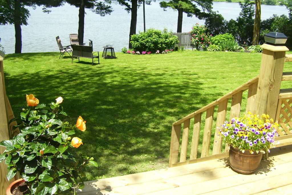 A new wooden deck with potted flowers leading down to a sunny lawn and garden