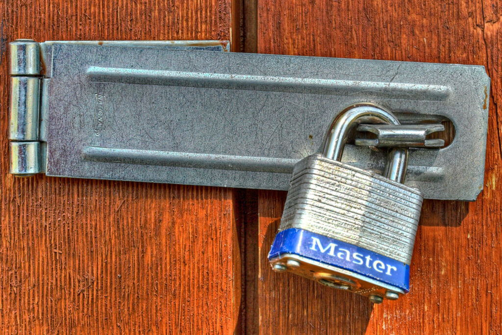 A steel padlock fastened through a hasp on a weathered red wooden door