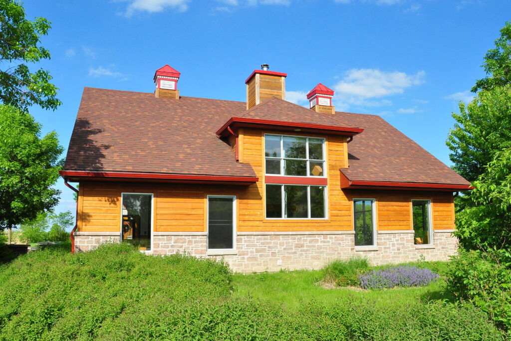 A timber-clad home with a new brown shingle roof and red chimney caps under a blue sky